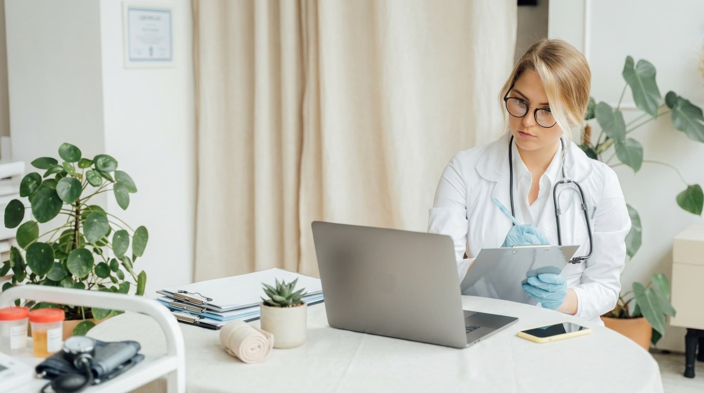 A doctor in a white coat reviewing notes on a clipboard at her desk